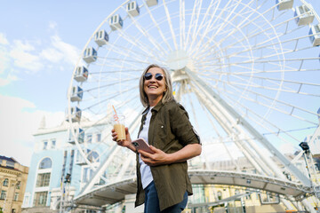 A woman standing in front of a colorful ferris wheel at an amusement park, looking up at the...