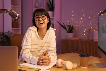 Young woman recording podcast in studio at night