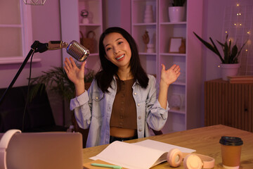 Young Asian woman recording podcast in studio at night