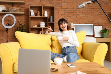 Young woman with coffee cup recording podcast at home