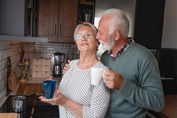 Beautiful senior married couple drinking coffee in the morning at home kitchen and sharing moment