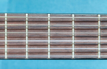 Close-up view of a guitar fretboard,  metal frets, strings against a blue background, object macro detail, extreme closeup, front view, frontal shot Classic acoustic guitar elements and parts up close