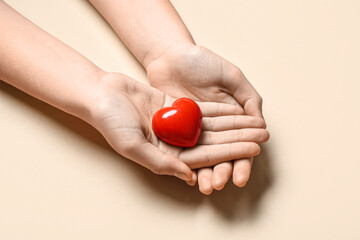 Female hands holding red heart on beige background