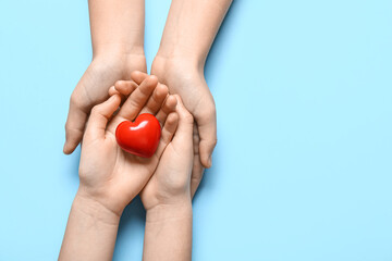 Hands of woman and child holding red heart on blue background