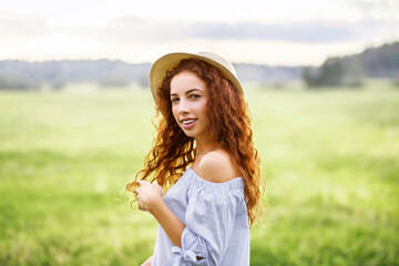 Summer portrait, beautiful freckled young woman wearing straw hat at sunset time on the field