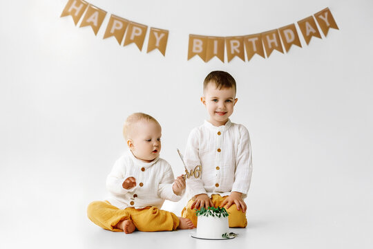 Two boys celebrating birthday, children have a B-day party. Birthday cake with candles and balloons. Happy kids, celebration, white minimalist interior.