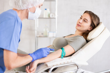 Experienced female doctor giving young woman injection in vein at hospital.