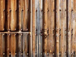Closeup of an antique rustic wooden exterior door with rusty iron rivets and a metal handle. Closed...