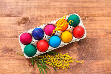 Paper holder with painted Easter eggs and mimosa flowers on wooden background