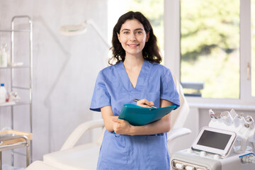 Female cosmetic doctor meticulously stands in her clinic, recording detailed notes in folder,...