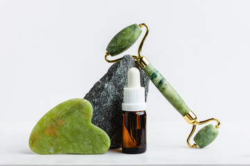 Green jade roller massager for face on white marble.