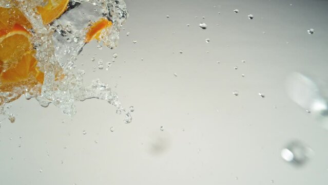 Super Slow Motion of Flying Orange Slices with Water Splashes, Isolated on Blue Background. Filmed on High Speed Cinema Camera, 1000fps.