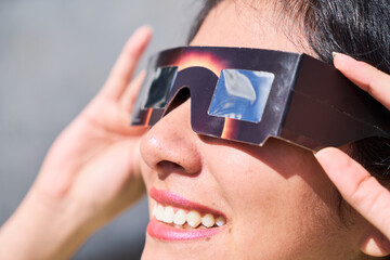 Smiling young latin woman watching an eclipse of the sun with eclipse glasses - obrazy, fototapety, plakaty