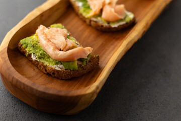 toast with cream cheese, avocado and salmon on a wooden plate, dark background