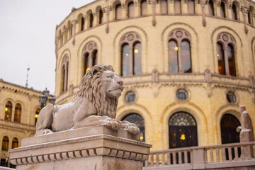 Fotobehang Statue of a lion in front of the house of norwegian parliament on a cold winter day. Lion peacefully resting on a pillar in front of majestic building. © Anze