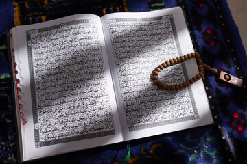 Close-up of wooden prayer beads lying on top of the open Quran