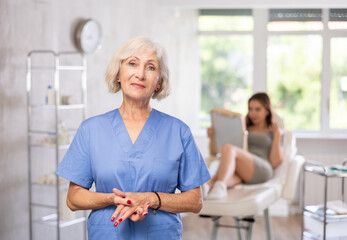 Portrait of elderly female doctor standing in light treatment room at beauty clinic