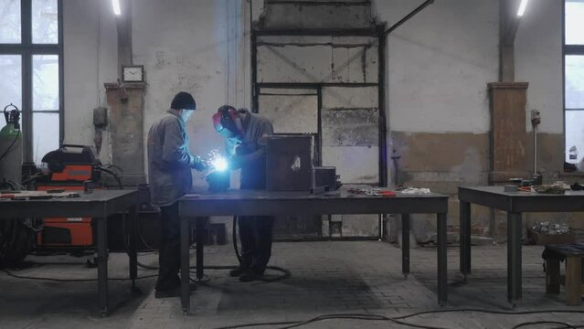 The workers in protective masks welding and grinding metal parts