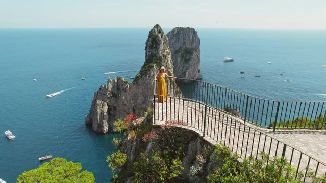 Tourist woman overlooks sea from Capri Island. A visitor enjoying breathtaking seaside panorama from viewpoint atop a craggy coast. Italy.