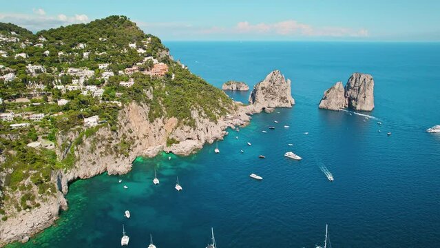 Capri coastline shines with Mediterranean nature under the summer sun. The high cliffs Faraglioni of Island and deep blue sea in Italy.