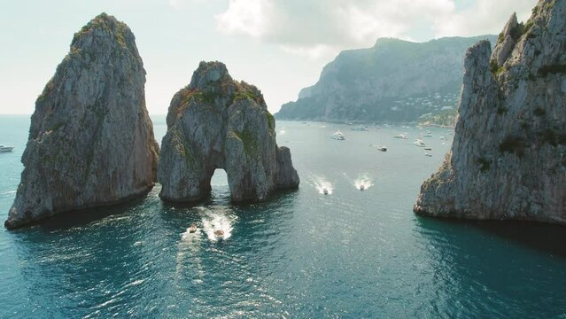 The towering sea stacks Faraglioni serve as a natural gateway, framing the lively waterway trafficked by boats of all sizes. Serene blue of the Mediterranean seascape in Capri, Italy.