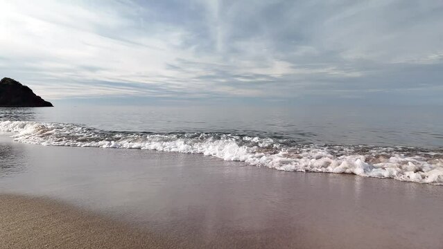Beautiful dark turquoise sea with white, foamy waves hitting the beach sand. Beautiful bright sunset and sea.