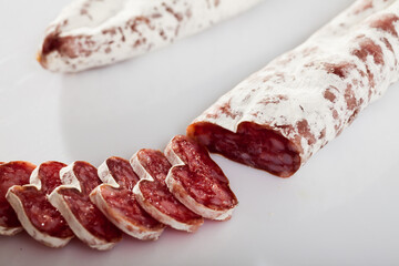 Sliced Catalan dry cured sausage Fuet on white background. Preferred Spanish meat products ..