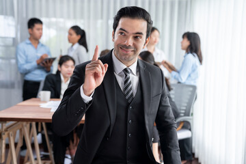 Portrait of happy businessman looking at camera, making finger pointing gesture for advertising product with motion blur background of business people movement in dynamic business meeting. Habiliment