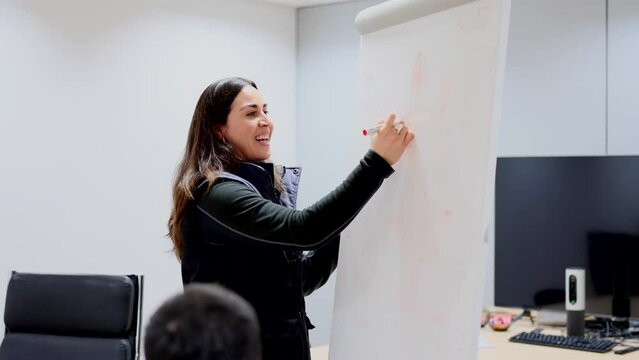 Young engineer woman writing on a whiteboard during a meeting. Person leading team.