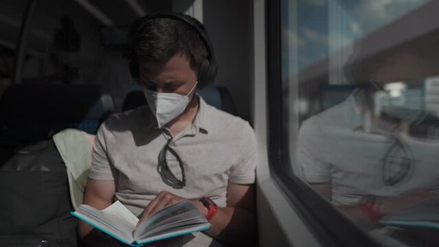 Passenger traveling on Deutsche train in summer with wireless headphones and reading book. Student reads study workbook with wireless earphones while commuting on train. Daily commute to university. 