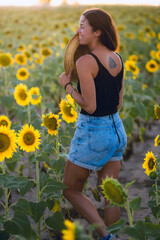 Young woman from behind looking at camera in a sunflower plantation during golden hour