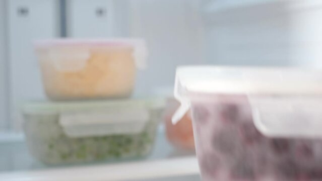 Female hand takes out glass box of blueberries from the refrigerator, front view.