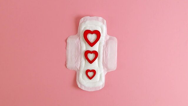 One feminine pad and three red hearts on pink.