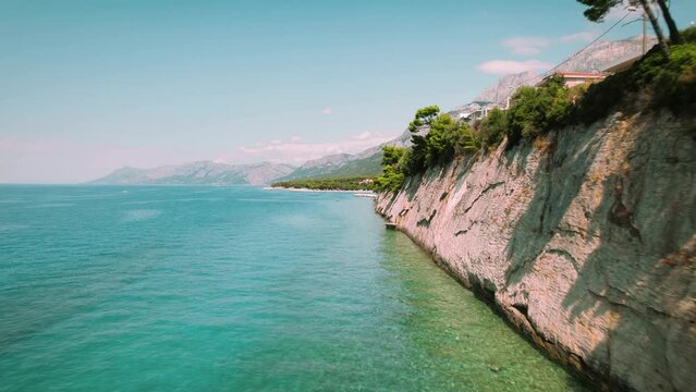 Cliffside along a calm sea, with layers of geological history. Vegetation clings to rocky outcrops above a secluded pebble beach. Aerial view of nature in summer Croatia.