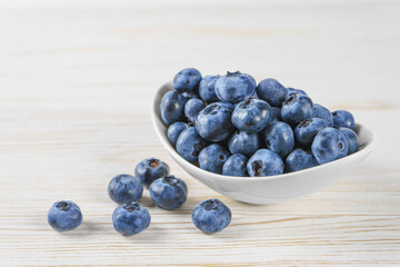 Fresh blueberries in a small round white bowl with scattering of berries on white wooden...