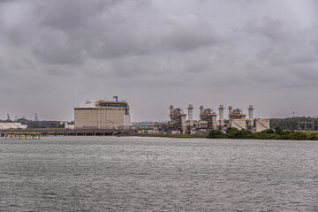 Fototapeta premium Port of Colon, Panama - July 24, 2023: AES Colon power station or Termoelectrica, heavy industry, buildings and installations to turn coal and gas into heat and electricity under gray cloudscape