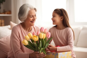 Fototapeta na wymiar International Women's Day. Smiling daughter and granddaughter giving flowers and gifts to grandma celebrating the holiday.
