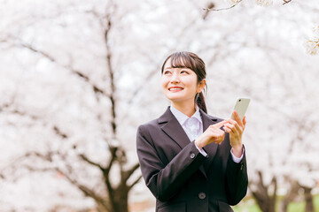 満開の桜の下にいるスーツ姿の女性（スマホ・SNS・投稿）
