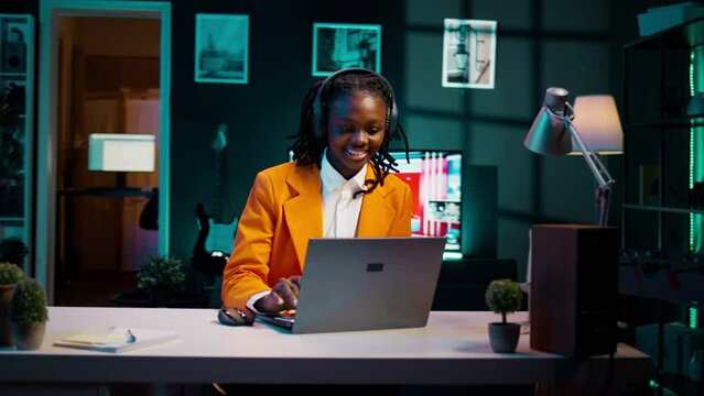 African american girl jamming on music and writing reports for her final bachelor essay, having fun with songs on headset. Student preparing for exams with class notes and materials. Camera B.