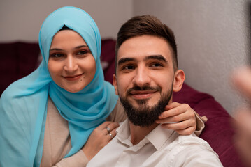 Happy Muslim Couple Making Selfie On Smartphone Sitting On Couch At Home.