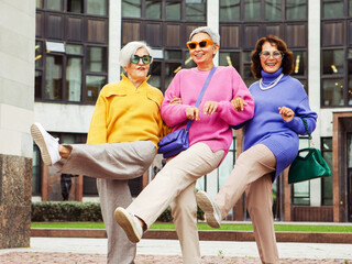 Three happy cheerful pensioner girlfriends in bright sweaters and sunglasses walk together