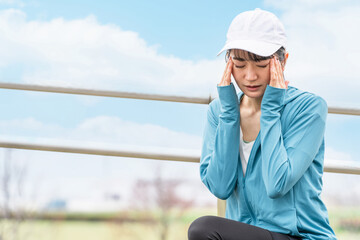 ランニング・ウォーキング中に頭痛・偏頭痛で困るスポーツウェアのアジア人女性
