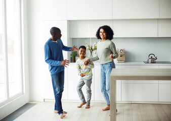 Cheerful afro american family - mom, dad and son dancing at home. Happy together.