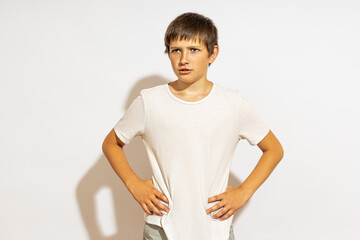 A teenager in a white T-shirt, resting his hands on his sides, looks to the side.