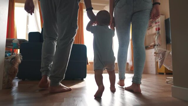 baby with parents first steps. happy family kid dream concept. baby son takes first steps holds family hands silhouette against window indoors. cute baby toddler learning lifestyle walk with family
