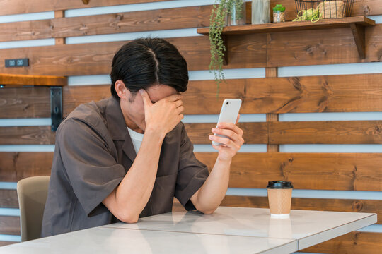 カフェ・家などでスマホを使う若いアジア人男性（落ち込む・失敗・悩む・困る・自己嫌悪）
