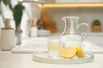 Fototapeta na wymiar Jug, glass with clear water and lemons on white table in kitchen, space for text