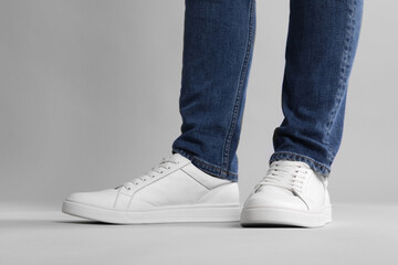 Man wearing stylish white sneakers on grey background, closeup