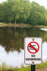 No swimming sign in front of lake with reflection of trees in the water.
