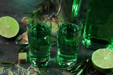 Absinthe in shot glasses, lime, rosemary and sugar on gray table, closeup. Alcoholic drink